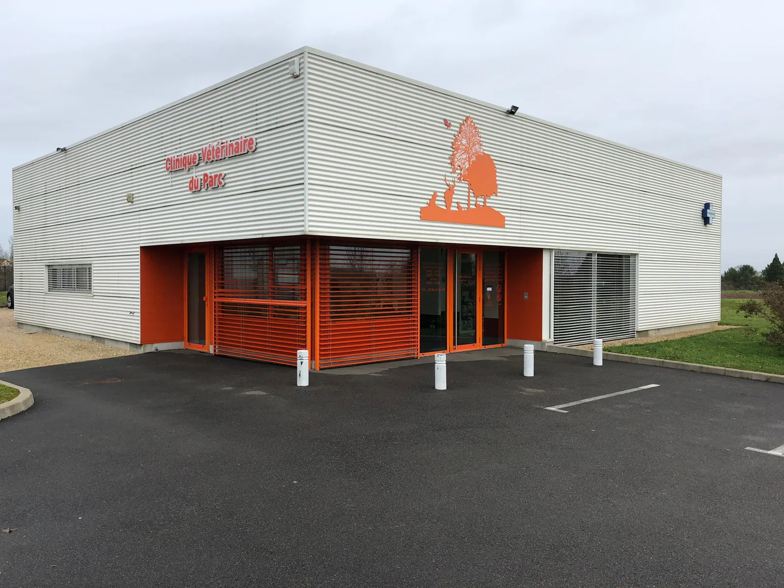Façade de la Clinique Vétérinaire du Parc à Villeneuve-la-Guyard : bâtiment blanc à bardage métallique, entrée orange, logo à l'arbre et aux animaux, parking devant la porte